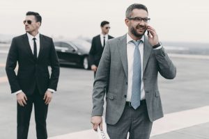 smiling businessman walking with bodyguards and talking by smartphone